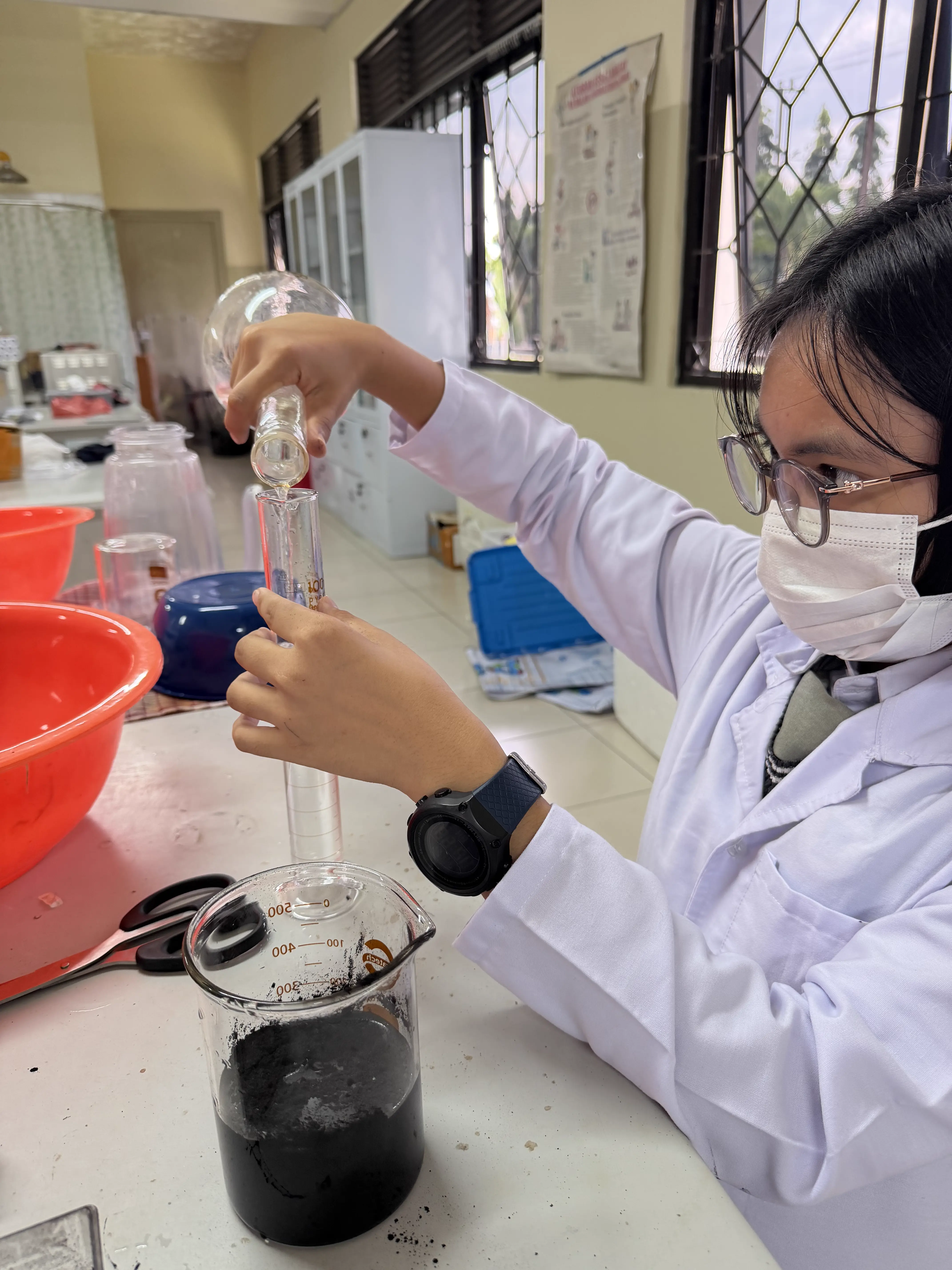 Peneliti muda berjas lab menuangkan larutan ke dalam gelas ukur